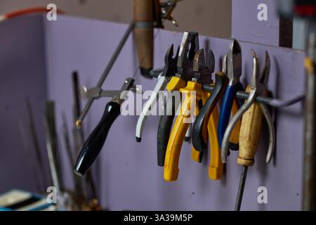 Various hand tools hanging neatly on hooks in an organized workshop setup with purple walls and a compact working environment ideal for tasks without clutter Stock Photo