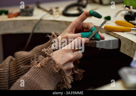 Hands wearing gloves while crafting on workbench with various tools. Focus on meticulous detail and precision of the work being performed in workshop Stock Photo