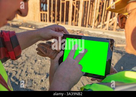 Construction Workers At Construction Site Holding Computer Tablet With Green Screen. Stock Photo