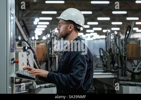 Using equipment, operator. Factory worker is indoors with hard hat. Stock Photo