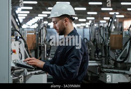 Using equipment, operator. Factory worker is indoors with hard hat. Stock Photo