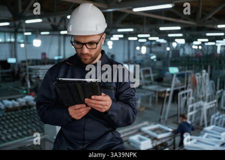 Reading the data from tablet. Factory worker is indoors with hard hat. Stock Photo