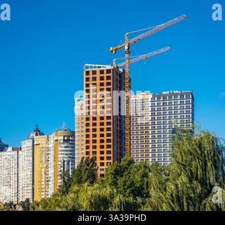 A bustling construction site dominates the urban skyline, featuring a yellow crane and emerging high-rise buildings against a vibrant blue backdrop. Stock Photo