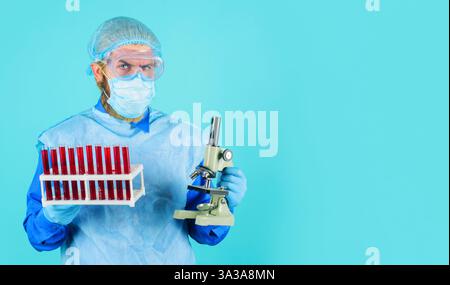 Male doctor with blood samples in test tubes and microscope in clinical laboratory. Blood test. Lab assistant in medical mask, safety glasses and glov Stock Photo