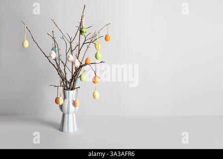 Vase with tree branches and colorful Easter eggs on white background Stock Photo