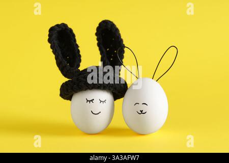 Funny Easter eggs with drawn faces in bunny ears on yellow background Stock Photo