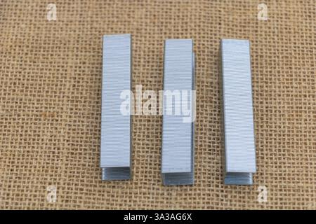 Three silver carpentry nails laying on a burlap background, top view. Stock Photo