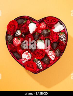 Luxurious heart-shaped box overflowing with red roses, chocolate strawberries, and raspberries. A stunning gift arrangement Stock Photo