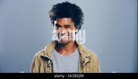 Man, smile and wink in studio with portrait, sign or emoji for secret, flirting and afro by gray background. Person, model and happy with icon, style Stock Photo