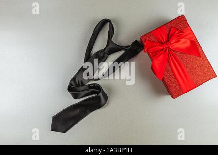 A stylish black tie is elegantly placed beside a vibrant red gift box adorned with a large bow. This scene captures the essence of Father's Day celebr Stock Photo