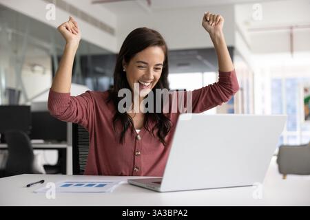 Happy Latin businesswoman making winner hands at laptop Stock Photo