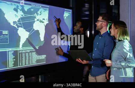 Black guy showing place on the map. Male business trainer is against projector with data, teaching people. Stock Photo