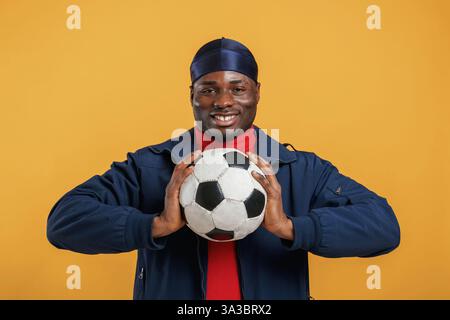 Holding soccer ball. Handsome black man is in the studio against yellow background. Stock Photo