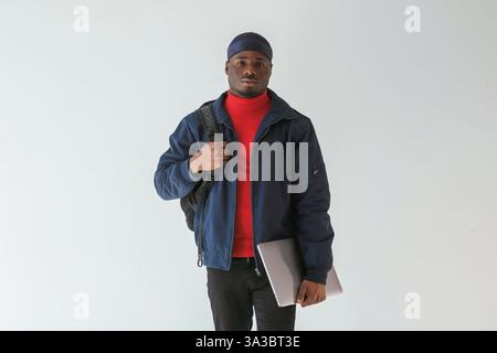 Silver colored laptop in hand. Black man in cap is in the studio against white background. Stock Photo