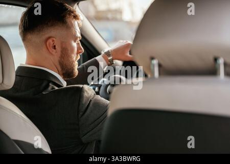 Driving, focused. Man in black suit is sitting in the car, driving. Stock Photo