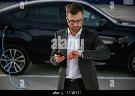 Handsome smart guy in glasses. Businessman in suit is near his black car outdoors. Stock Photo