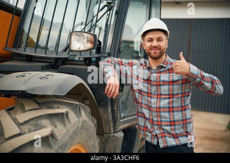 Leaning on the vehicle. Man is with tractor. Agricultural worker. Stock Photo