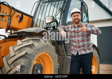 Leaning on the vehicle. Man is with tractor. Agricultural worker. Stock Photo