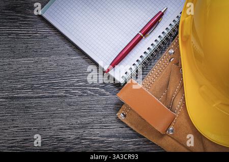 Toolbelt building helmet checked notepad ball-point pen on wooden board construction concept Stock Photo
