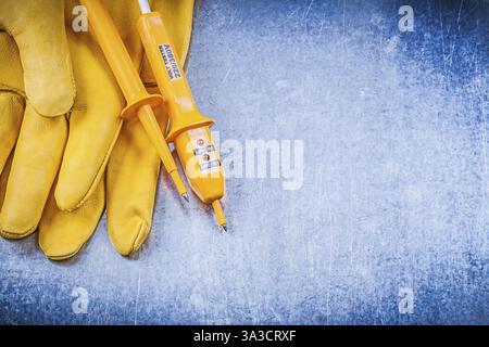 Yellow electrical tester safety gloves on metallic background electricity concept Stock Photo