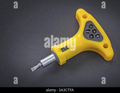 Yellow reversible screwdriver wih bits on black background Stock Photo