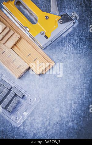 Yellow construction stapler chrome staples wooden building board on metallic background Stock Photo
