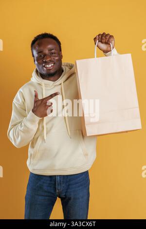 Bag with copy space, conception of shopping. Black guy is against yellow background. Stock Photo