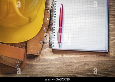 Tool belt building helmet checked copybook ball-point pen on wooden board construction concept Stock Photo