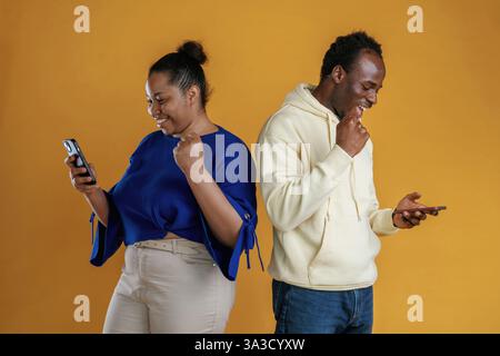 Using smartphones. Happy black couple are together against yellow background. Stock Photo