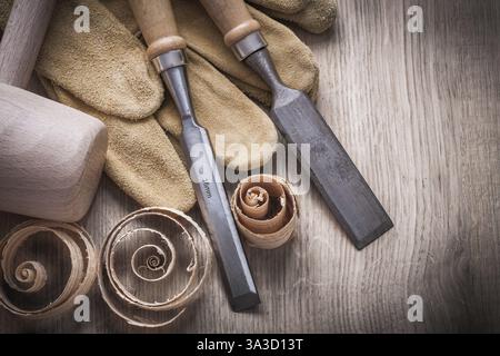 Wooden mallet curled up planning chips firmer chisels leather gloves on wood board construction concept Stock Photo