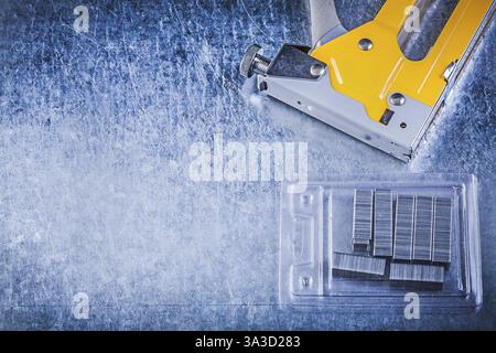 Yellow stapler gun chrome staples on scratched metallic background Stock Photo