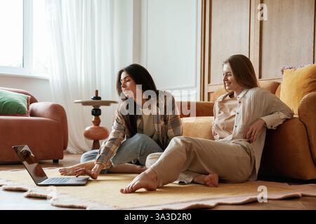 Watching movie by using laptop. Two happy young female best friends are indoors. Stock Photo