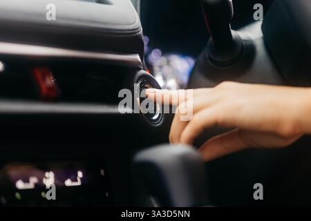 Close-up of a car start button being pressed by a woman. Concept of modern technology, convenience, and innovation in cars. Stock Photo