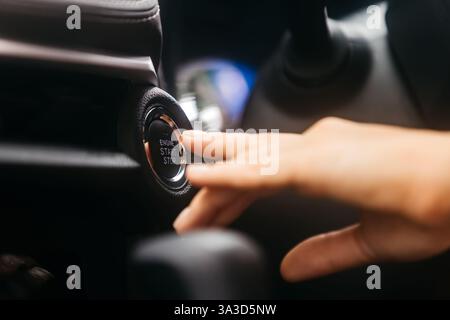Close-up of a car start button being pressed by a woman. Concept of modern technology, convenience, and innovation in cars. Stock Photo