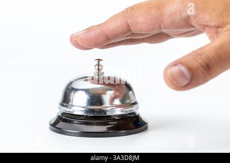 Close-up of a shiny silver service bell and a chubby hand reaching out to ring it. Stock Photo