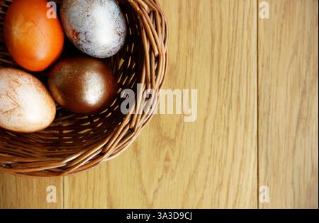 Four Easter eggs painted in different shades of brown color lying in a wicker basket on wooden background. Simple Easter flat lay in neutral colors Stock Photo