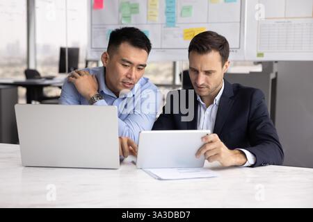 Busy Asian and Caucasian male business colleagues discussing software product Stock Photo