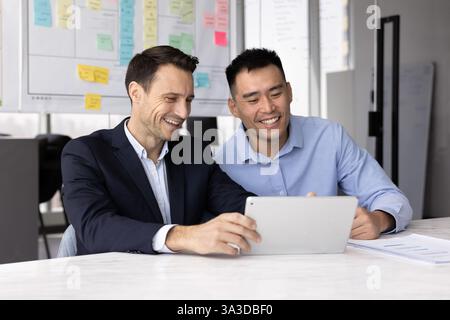 Happy diverse male businessmen using tablet computer at workplace together Stock Photo
