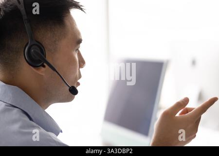 Serious Asian telemarketing employee man in headset talking to client Stock Photo