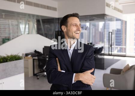Happy CEO standing in modern office alone with hands crossed Stock Photo