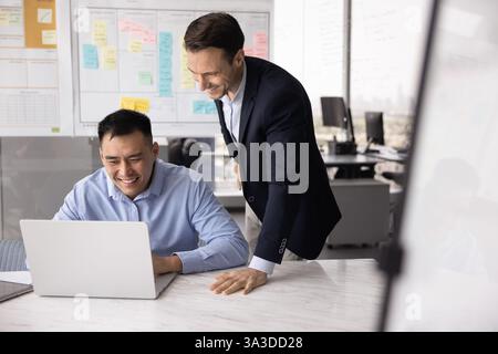 Happy male Caucasian boss checking positive Asian manager work process Stock Photo