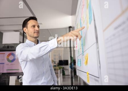 Positive focused Hispanic businessman pointing at post it sticky notes Stock Photo