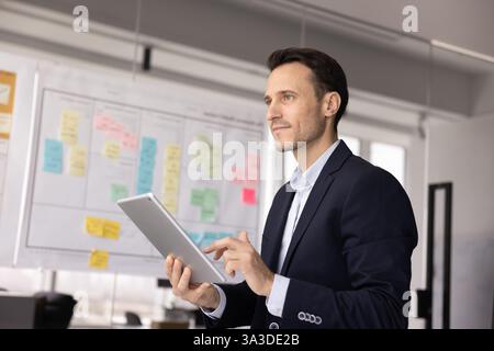 Confident thoughtful Latin CEO man working on tablet and thinking Stock Photo