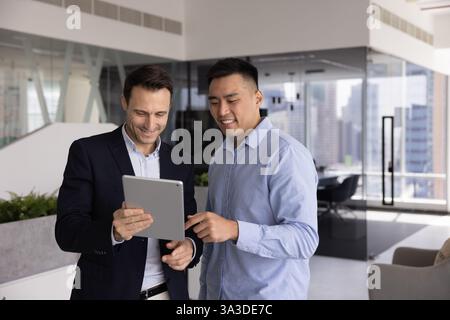 Two positive multiethnic businessmen standing with digital gadget in office Stock Photo
