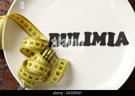 Plate with word Bulimia, fork and measuring tape on wooden table, top view Stock Photo