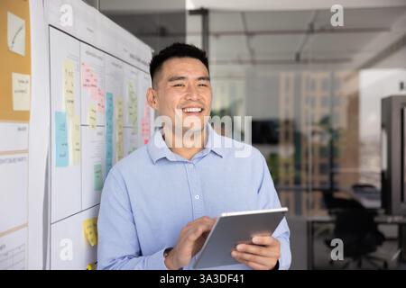 Positive successful Asian project manager working with tablet Stock Photo