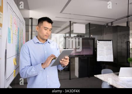 Focused young Asian manager man using modern technology on tablet Stock Photo