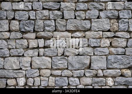Stone wall is constructed with uneven, rough-cut gray stones. Detail of traditional stone masonry from the South of France in the Seguret village. Stock Photo