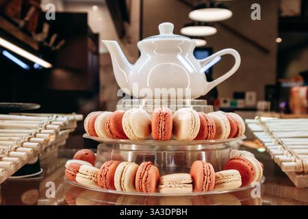 A display of delicious macarons with a teapot, arranged on a glass stand in a cafe setting Stock Photo