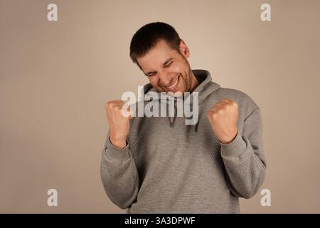 This victorious gesture reflects a moment of success and personal achievement. Ideal for moments of triumph. The man, with a wide grin, lifts his Stock Photo